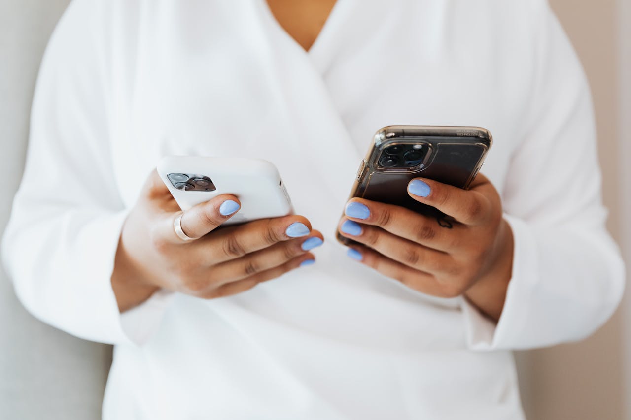 digital A person with blue nail polish holds two smartphones, showcasing modern technology.